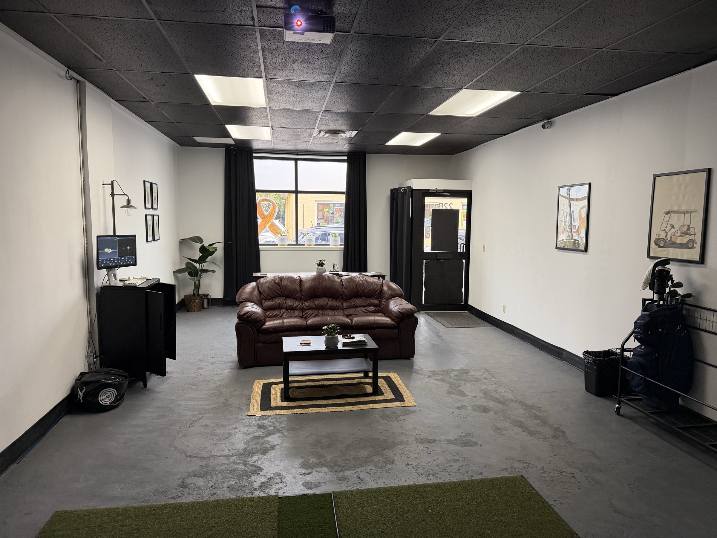 Lounge area inside Dev's Golf Sim in Essex, Ontario, with a leather couch, coffee table and a golf bag on a rack